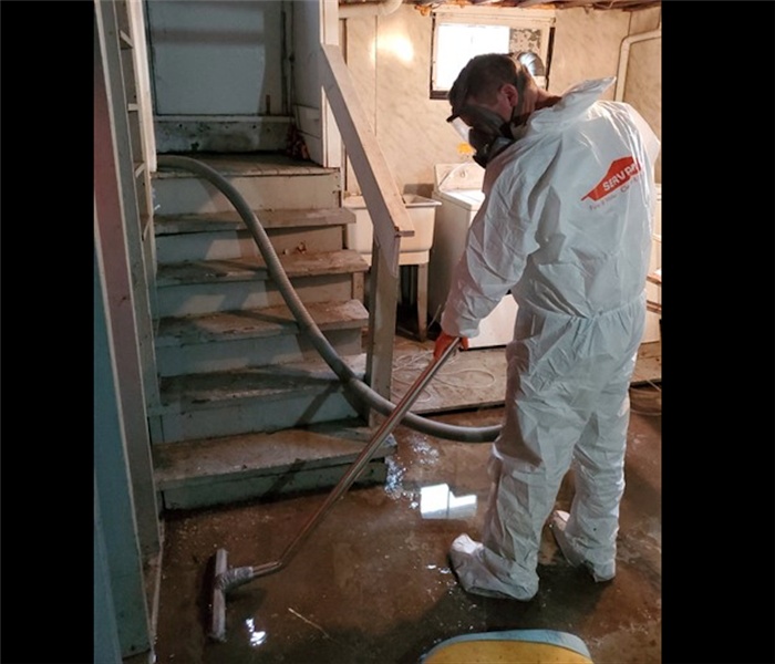 SERVPRO technician in white PPE extracting water from concrete basement