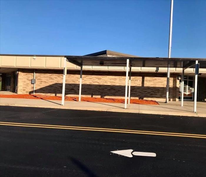 Brick building with blue sky behind and black parking lot with arrow in front of it