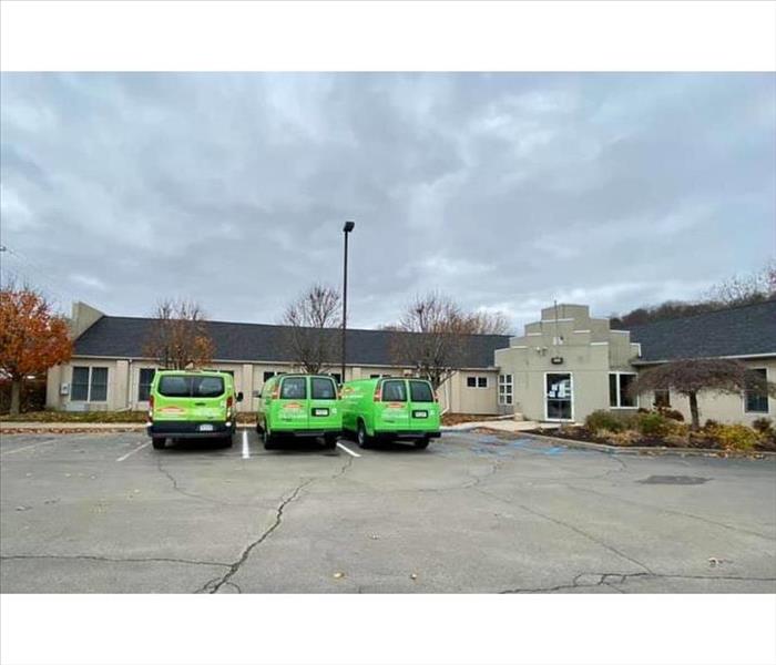 Three green SERVPRO trucks in front of building 